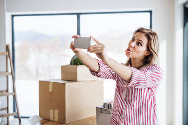 A joyful woman captures a selfie with her smartphone while settling into her new home, making a funny face - HPIF26026