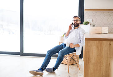 A mature man with coffee and smartphone moving in new home, making a phone call. - HPIF26043