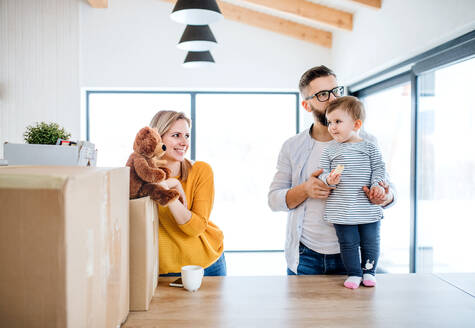 Ein Porträt einer glücklichen jungen Familie mit einem kleinen Mädchen, das in ein neues Haus einzieht. - HPIF26070