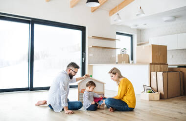 Ein Porträt einer glücklichen jungen Familie mit einem Kleinkind, das in ein neues Haus zieht und spielt. - HPIF26077