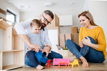 Ein Porträt einer glücklichen jungen Familie mit einem Kleinkind, das in ein neues Haus zieht und spielt. - HPIF26078