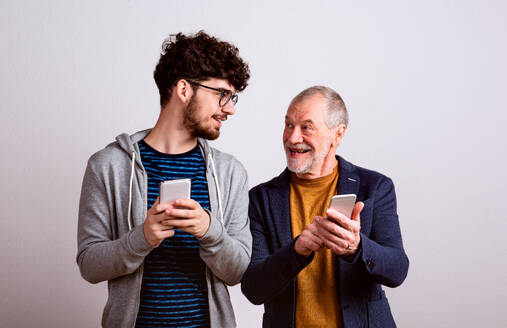 Ein Porträt eines älteren Vaters und eines jungen Sohnes in einem Studio, mit Smartphone. - HPIF26098