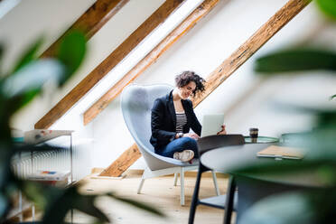 Eine junge Geschäftsfrau mit Laptop sitzt am Tisch im Büro und arbeitet. - HPIF26105