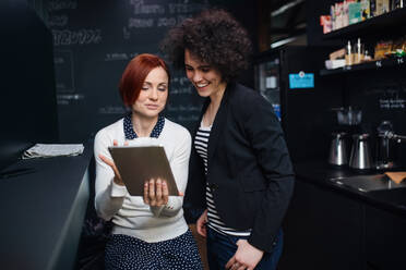 Two young cheerful female businesspeople using tablet in office, start-up concept. - HPIF26112