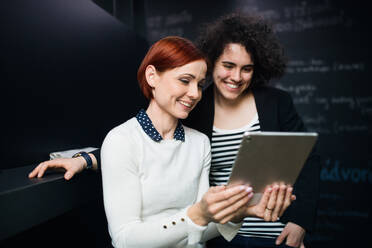 Zwei junge, fröhliche Geschäftsfrauen benutzen ein Tablet im Büro, Start-up-Konzept. - HPIF26113