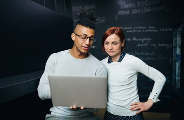 Two young cheerful businesspeople using laptop in office, start-up concept. - HPIF26114