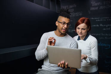 Two young cheerful businesspeople using laptop in office, start-up concept. - HPIF26115