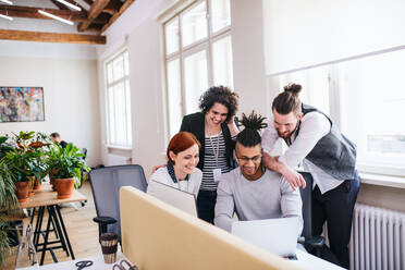 A group of young cheerful businesspeople using laptop in office, start-up concept. - HPIF26141