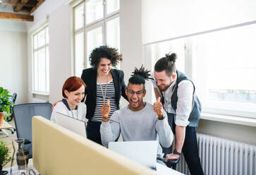Eine Gruppe junger, fröhlicher Geschäftsleute, die einen Laptop im Büro benutzen, Start-up-Konzept. - HPIF26142