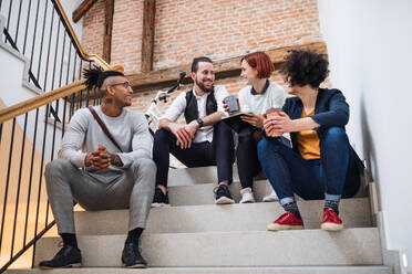 Eine Gruppe junger Geschäftsleute sitzt auf einer Treppe im Haus und unterhält sich über ein Start-up-Konzept. - HPIF26155