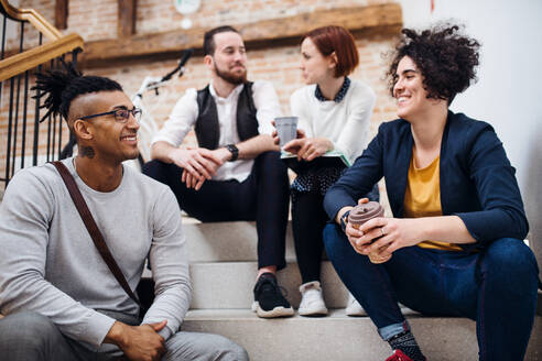 Group of young businesspeople sitting on stairs indoors, talking. A start-up concept. - HPIF26156