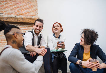 Group of young businesspeople sitting on stairs indoors, talking. A start-up concept. - HPIF26157