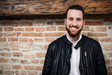 A happy young businessman standing outdoors against brick wall. Copy space. - HPIF26163