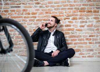 A young businessman with bicycle and telephone sitting on the floor in office, making a phone call. - HPIF26164