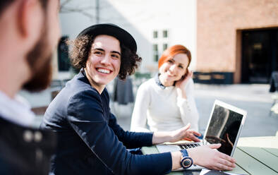 Junge Geschäftsleute mit Laptop im Freien im Innenhof, lachend. Start-up-Konzept. - HPIF26183