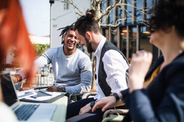 Junge Geschäftsleute mit Laptop im Freien im Innenhof, lachend. Start-up-Konzept. - HPIF26184