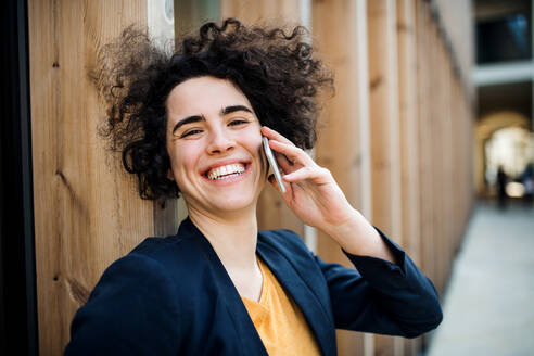 Eine glückliche junge Geschäftsfrau mit Smartphone, die im Freien steht und einen Anruf tätigt. - HPIF26215