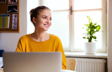 Eine junge, glückliche Studentin, die zu Hause am Tisch sitzt und einen Laptop benutzt, um zu lernen. - HPIF26234