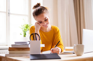 A young happy college female student sitting at the table at home, studying. - HPIF26236