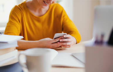 Ein Mittelteil eines jungen glücklichen College-Studenten, der zu Hause am Tisch sitzt und beim Lernen sein Smartphone benutzt. - HPIF26238
