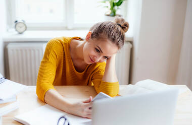 A young happy college female student sitting at the table at home, using laptop and smartphone when studying. - HPIF26240