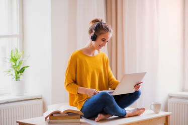 A young happy college female student sitting at the table at home, using headphones and laptop when studying. - HPIF26247