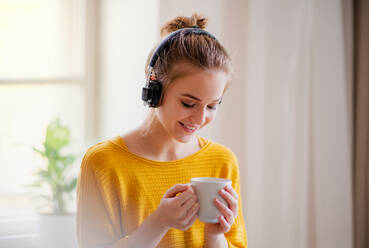 Eine junge, glückliche Studentin sitzt zu Hause am Tisch und benutzt beim Lernen Kopfhörer. - HPIF26250