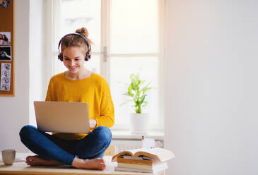 Eine junge, glückliche Studentin sitzt zu Hause am Tisch und benutzt Kopfhörer und Laptop beim Lernen. - HPIF26252