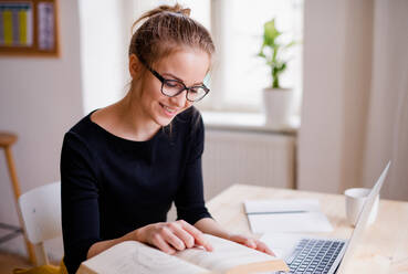 Eine junge, glückliche Studentin, die zu Hause am Tisch sitzt und einen Laptop benutzt, um zu lernen. - HPIF26256