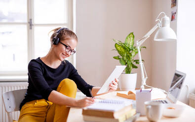 A young happy college female student sitting at the table at home, using tablet and headphones when studying. - HPIF26263