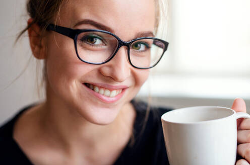 Nahaufnahme eines Porträts einer glücklichen jungen Studentin, die eine Tasse Kaffee in der Hand hält. - HPIF26269