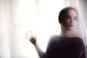 A silhouette of young sad woman standing by window. Copy space. - HPIF26277