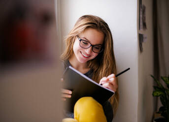 Eine junge, glückliche Studentin mit einem Schulheft, die zu Hause auf der Fensterbank sitzt und lernt. - HPIF26282