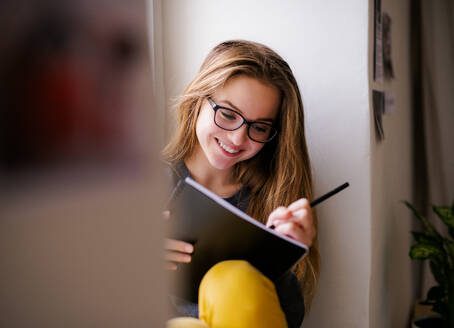 Eine junge, glückliche Studentin mit einem Schulheft, die zu Hause auf der Fensterbank sitzt und lernt. - HPIF26282