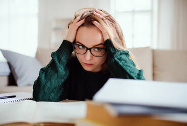 A young unhappy and sad college female student sitting at the table at home, studying. - HPIF26289