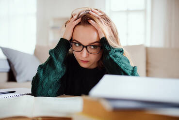 Eine junge, unglückliche und traurige Studentin sitzt zu Hause am Tisch und lernt. - HPIF26289