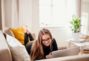 Eine junge, glückliche Studentin, die zu Hause auf dem Sofa liegt und einen Laptop benutzt, um zu lernen. - HPIF26312