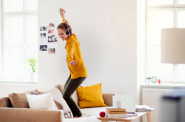 Eine junge Studentin mit Kopfhörern und Telefon macht eine Pause beim Lernen und tanzt auf dem Sofa. - HPIF26318
