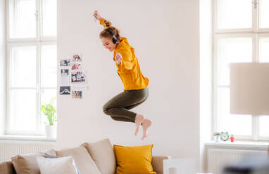 Eine junge Studentin mit Kopfhörern und Telefon macht eine Pause beim Lernen und hüpft auf dem Sofa. - HPIF26319