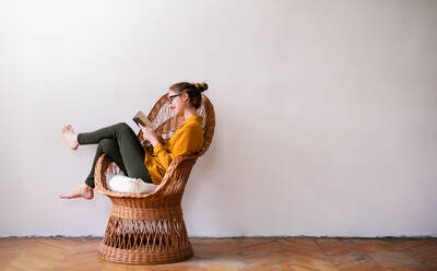 A happy young female student sitting on wicker chair, reading. Copy space. - HPIF26326