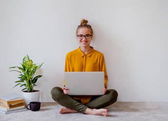 A young college female student sitting on floor at home, using laptop when studying. - HPIF26328