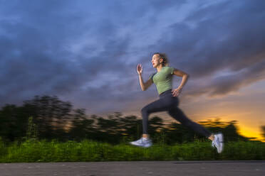 Young athlete sprinting on footpath at dusk - STSF03714