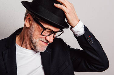 Portrait of a senior man with hat and glasses in a studio, looking down. - HPIF26338