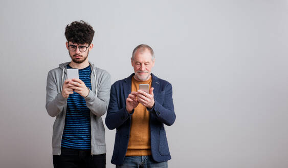 Ein Porträt eines älteren Vaters und eines jungen Sohnes in einem Studio, mit Smartphone. - HPIF26341