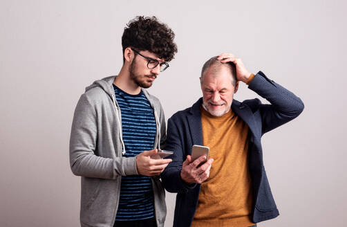 Ein Porträt eines älteren Vaters und eines jungen Sohnes in einem Studio, mit Smartphone. - HPIF26342