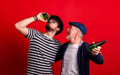 Young man and senior father with bottles in a studio on red background, drinking. - HPIF26350