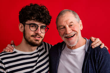 Vorderansicht eines jungen Mannes und eines älteren Vaters in einem Atelier auf rotem Hintergrund. - HPIF26352