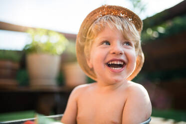 Ein kleiner Junge mit Hut im Freien oben ohne im Garten im Sommer, lachend. Kopierraum. - HPIF26360