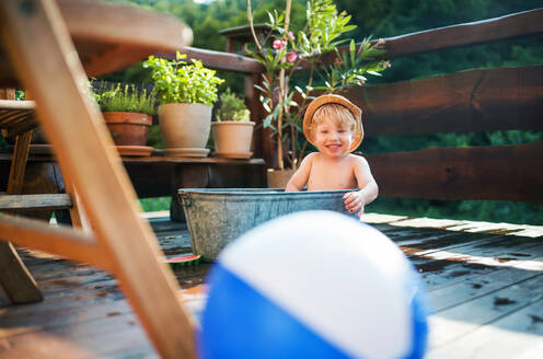 Glücklicher kleiner Junge mit einem Ball in der Badewanne im Freien im Garten im Sommer, spielen im Wasser. - HPIF26362