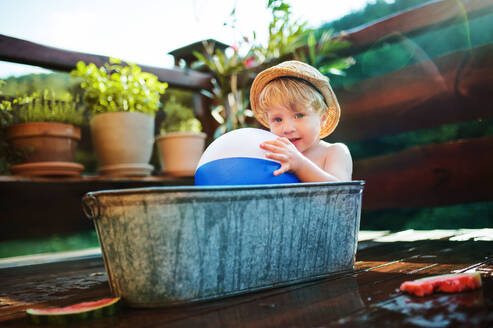 Glücklicher kleiner Junge mit einem Ball in der Badewanne im Freien im Garten im Sommer, spielen im Wasser. - HPIF26363
